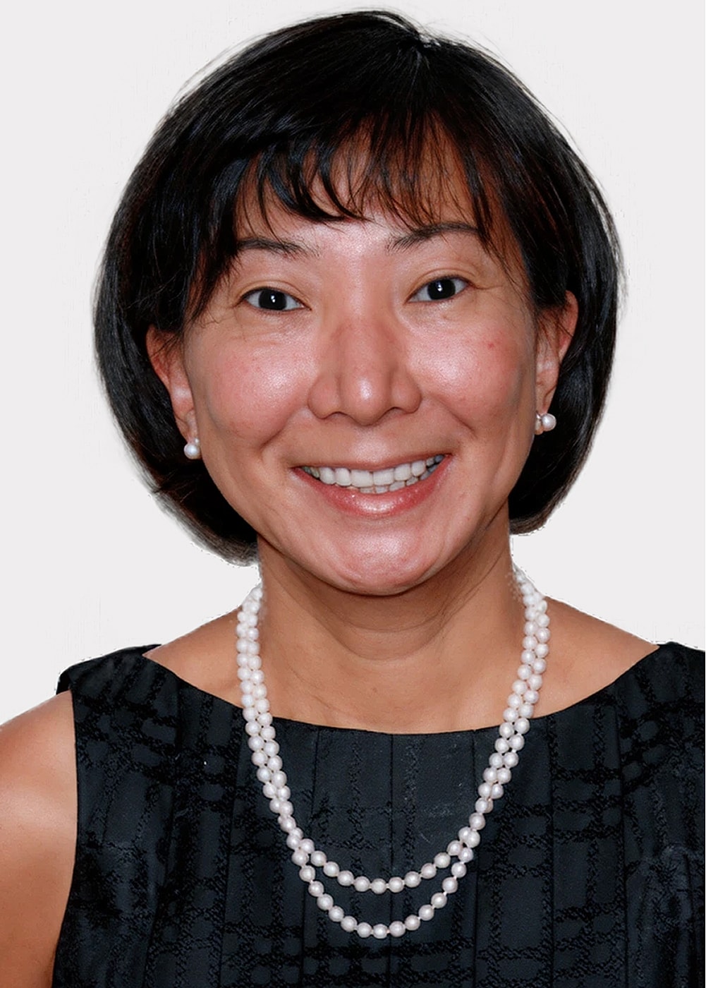 Smiling woman wearing pearls and black dress.