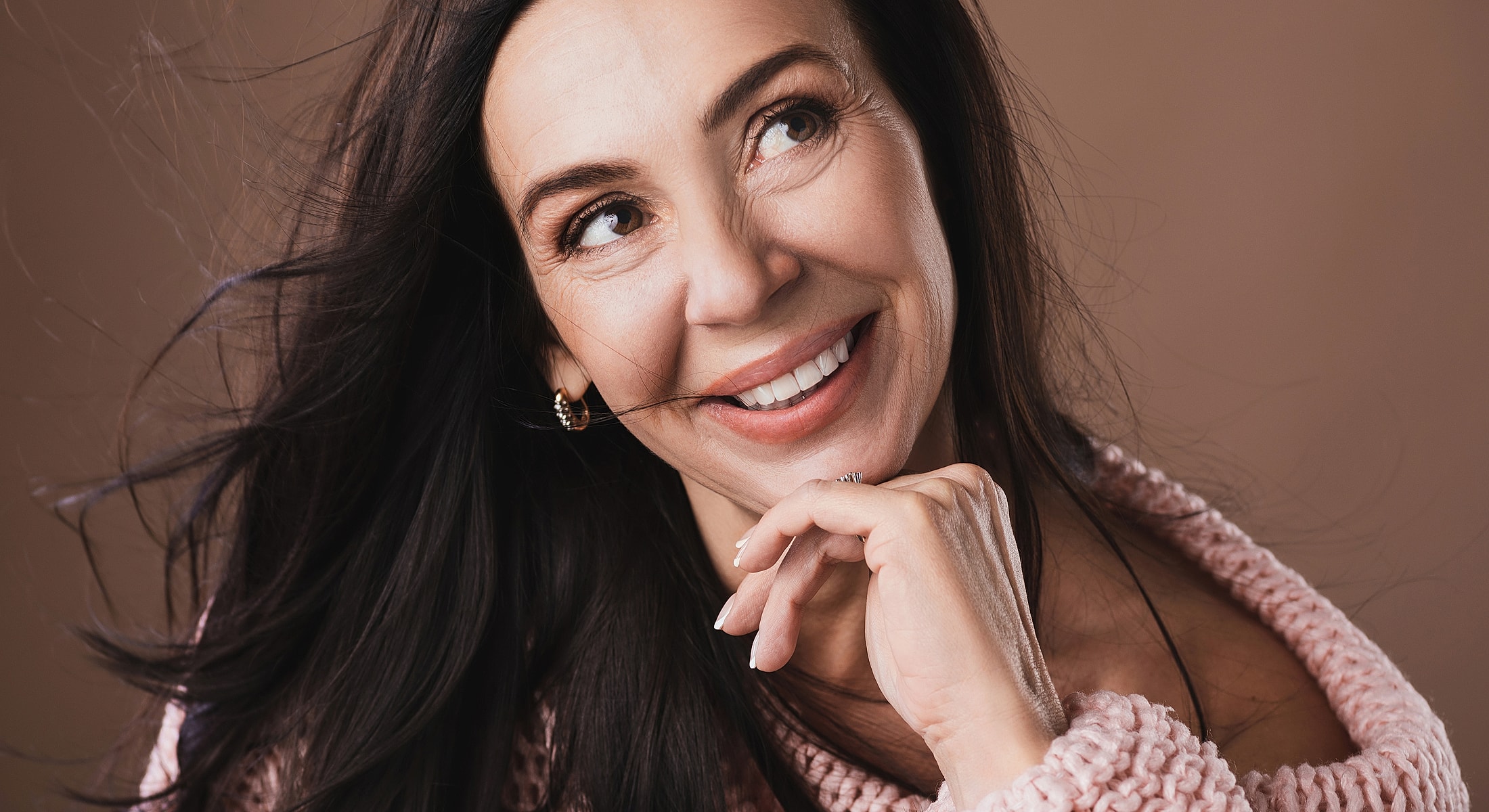 Smiling woman with flowing hair on brown background.